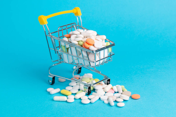 Medicinal antibiotic pills in shopping cart on blue background - Foto, afbeelding