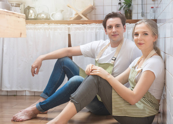 Jeune homme et femme caucasien heureux s'habiller dans le style de vie assis sur le sol dans la cuisine et parler. Aimer les jeunes couples passer du temps ensemble à la maison
. - Photo, image