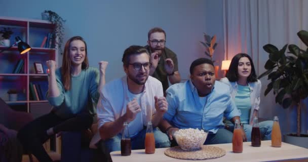 Group of excited sport fans supporting team while sitting on sofa near table with drinks and snacks. Group of friends become sad and disapointed while watching sport on TV. - Video