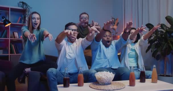 Excited group of friends cheering doing wave, applouding while sitting in front of TV. Happy people supporting team, giving high five and having fun while watching sport on TV. - Кадри, відео