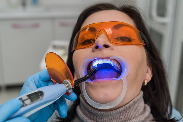Frau mit Schutzbrille sitzt im Zahnarztstuhl - Foto, Bild