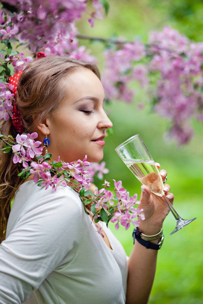 Beautiful female with glass of champagne in the sakura garden - Photo, Image