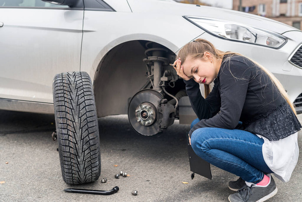 Woman in despair looking at spare wheel for car - Φωτογραφία, εικόνα
