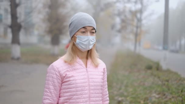 ヨーロッパの都市における中国のコロナウイルスからの保護。公共の場所で若い女性がドイツの医療マスクに立っています。コロナウイルスの症状の発症. - 映像、動画