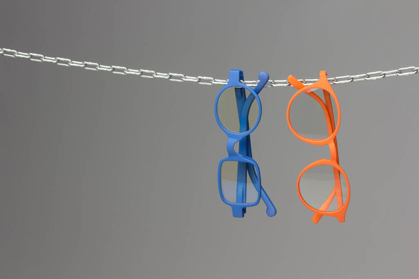 Colored glasses on a gray background and chain; glasses for vision correction; lenses to read or see from afar; Glasses can improve people's vision. - Photo, Image