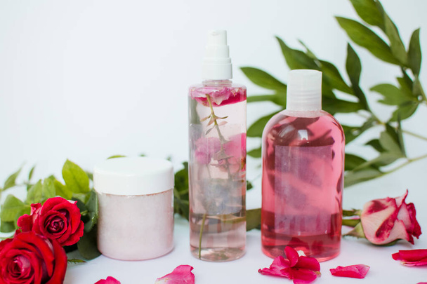 Kosmetikflaschen mit grünen Blättern und roten Rosen auf weißem Hintergrund. Natürliche Bio-Kosmetik mit pflanzlichen Inhaltsstoffen, Blumen. Etikett für Branding-Attrappe. Schönheits-, Gesundheits- und Pflegekonzept - Foto, Bild