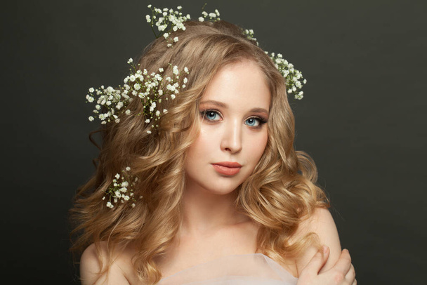 Mujer joven perfecta con flores blancas en pelo rubio sobre fondo oscuro
 - Foto, Imagen