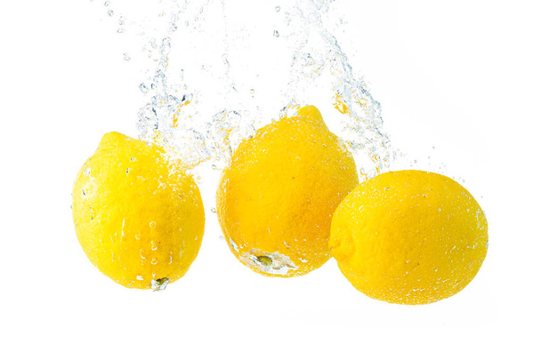 Lemons splash into water and sinking on white background. Tasty and healthy food - Фото, изображение