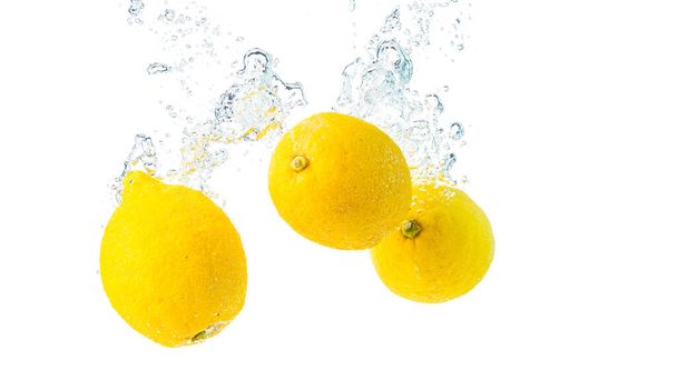 Citrony stříkají do vody a potápí se na bílém pozadí. Chutné a zdravé jídlo - Fotografie, Obrázek