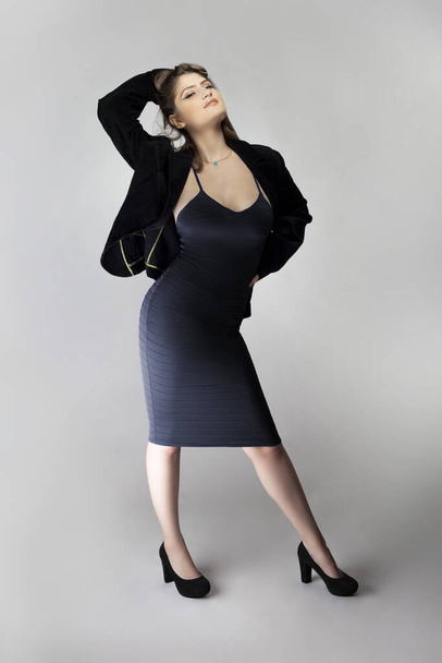 Female model posing as a sexy business woman looking confident like a boss or a manager. Her outfit is a trendy charcoal blue dress with a business suit or jacket.  - Фото, зображення