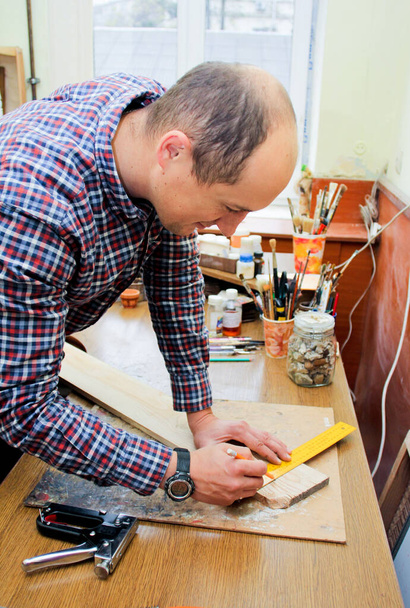 Un hombre trabaja en una carpintería, trabajando con un árbol. El hombre dibuja marcas en la madera con una regla
 - Foto, imagen