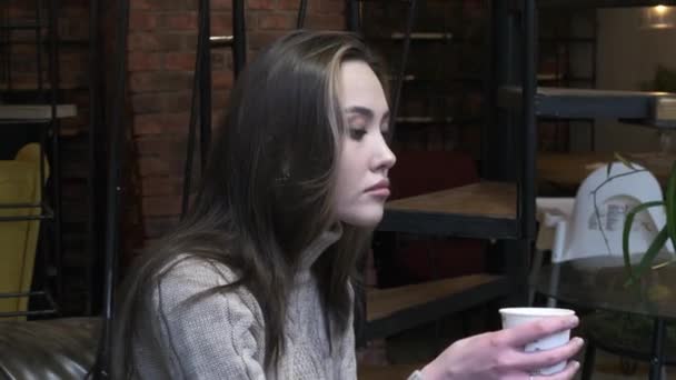 Stylish thoughtful young asian pretty girl sits at cafe, holds cup of coffee - Metraje, vídeo
