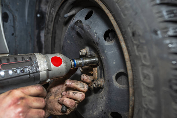 O mecânico do carro aparafusa a roda do carro de aço com uma chave pneumática em uma oficina do carro, mãos masculinas visíveis
. - Foto, Imagem