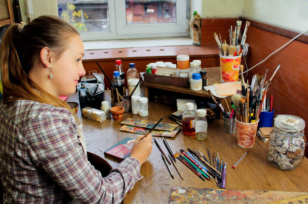 女の子アーティストがスタジオで絵を描く。聖ニコラスのアイコンの再現。スタジオでのアーティストのワークフロー。バックグラウンド・アート・ワークプレイスのブラシとペイント. - 写真・画像