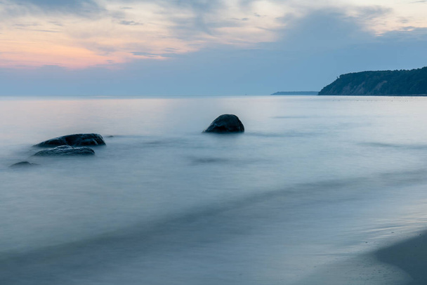 costa empinada en el horizonte, larga exposición superficie lisa del mar con grandes rocas que sobresalen del agua en el crepúsculo azul
 - Foto, imagen