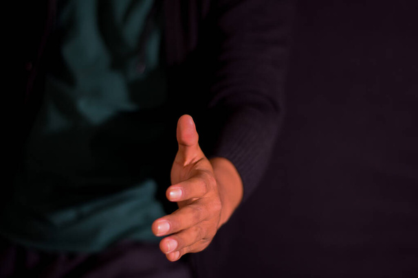 Young man giving hand for shaking on dark black background. selective focus on finger - Foto, Bild