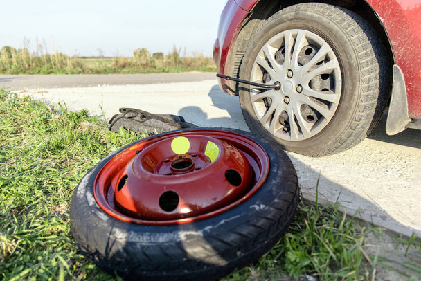 a flat tire near the car and a spare tire nearby - Photo, Image