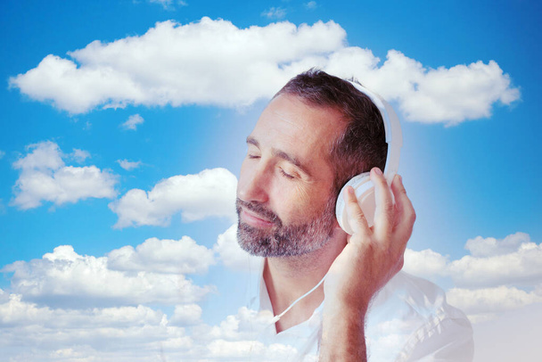 man with white headphones and a blue cloudy sky - Foto, Imagen