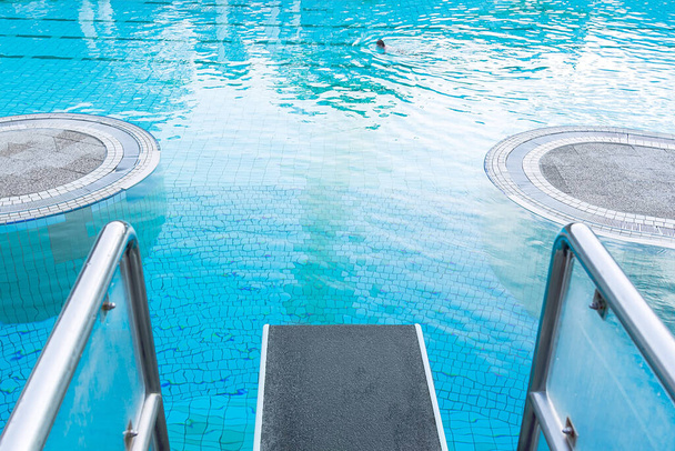 Vista superior close-up em uma prancha de mergulho contra o fundo de uma piscina com água azul em que uma pessoa nada. O conceito de verão, relaxamento, spa, parque aquático, esportes, arquitetura
 - Foto, Imagem