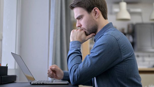 Νεαρός που σκέφτεται και εργάζεται σε φορητό υπολογιστή - Φωτογραφία, εικόνα