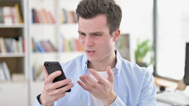 Расстроенный молодой человек получает шок на смартфоне
 - Фото, изображение