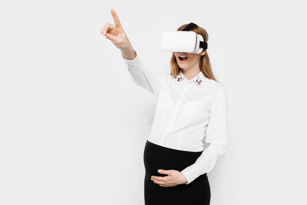 Image of a young pregnant businesswoman wearing virtual reality glasses, entertainment in the workplace, on a white background - Photo, image