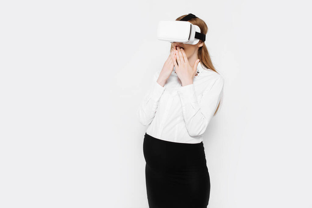 Image of a young pregnant businesswoman wearing virtual reality glasses, entertainment in the workplace, on a white background - Фото, изображение