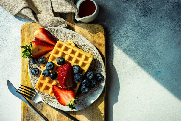 Traditional european breakfast with waffles, organic strawberry and blueberry on stone background with copy space - Foto, Imagen