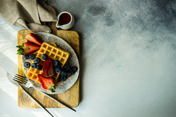 Традиционный европейский завтрак с вафлями, органической клубникой и черникой на каменном фоне с копировальным пространством
 - Фото, изображение