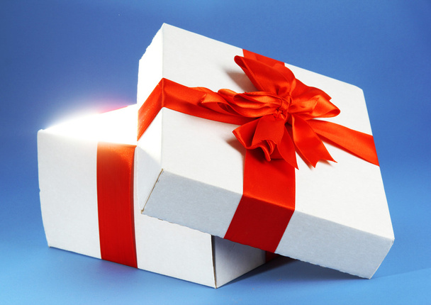 Gift box with bright light on it on blue background - Fotó, kép