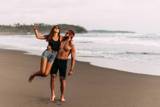 Happy couple having fun on the coast. A couple having fun on the beach in Indonesia. A man and a woman travel the world. Vacation in Bali. A couple in love meet the sunset on the sea. Travel to Asia - Foto, immagini
