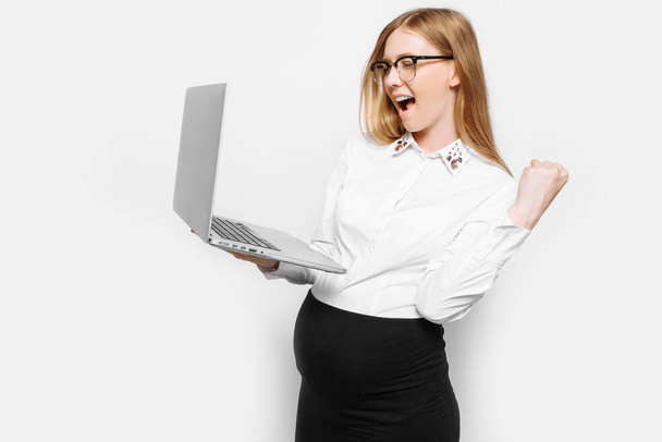 Image of a young pregnant businesswoman in glasses posing with a laptop, showing a gesture of victory and success , on a white background - Foto, imagen