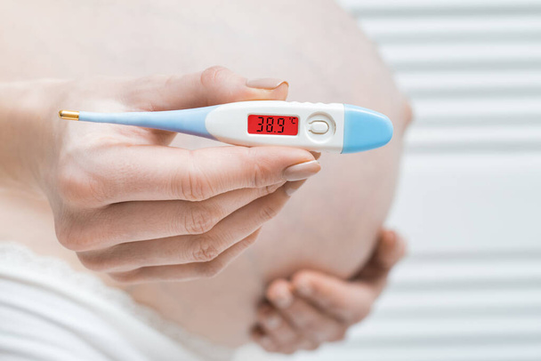 mujer embarazada con termómetro en la mano y alta temperatura. Enfermedades durante el concepto de embarazo
. - Foto, Imagen