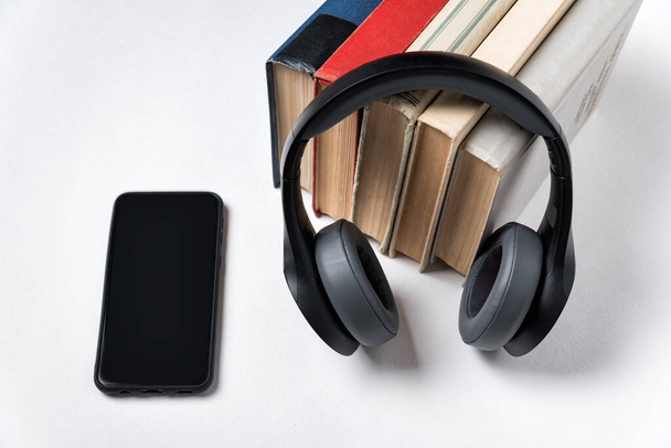 Pocos libros, auriculares y teléfonos inteligentes. Aprendizaje moderno con audio. Fondo blanco
. - Foto, Imagen