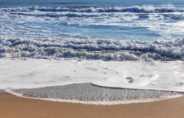 Ένα απαλό κύμα κυλάει στην άμμο της παραλίας. Θαλασσινά κύματα στην ακτή - Φωτογραφία, εικόνα