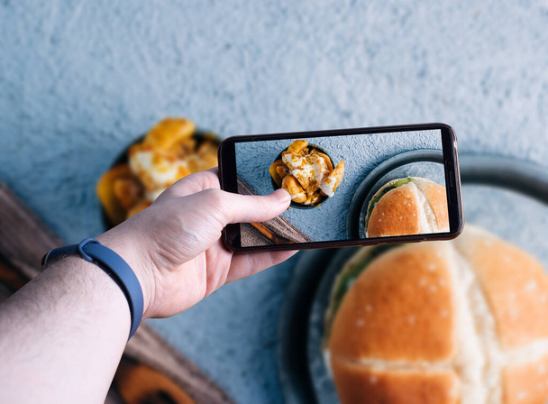 manos recogiendo un teléfono inteligente tomando una foto de una hamburguesa. Espacio para el texto. Enfoque selectivo
 - Foto, Imagen