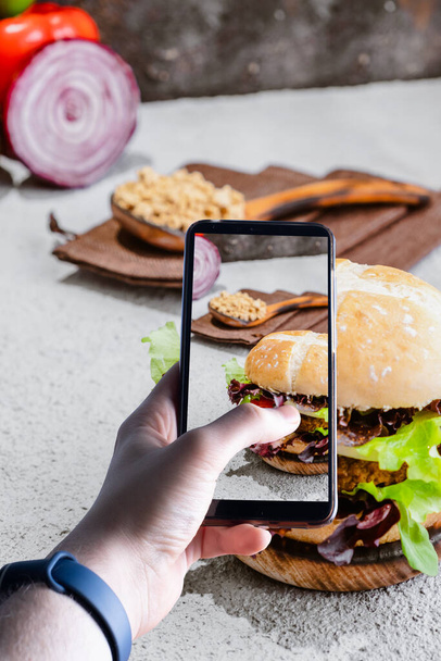 hands picking up a smartphone taking a picture of a burger. Space for text. Selective focus - Фото, изображение