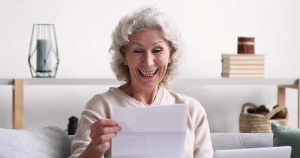 Cheerful old woman reads mail letter excited by good news - Séquence, vidéo