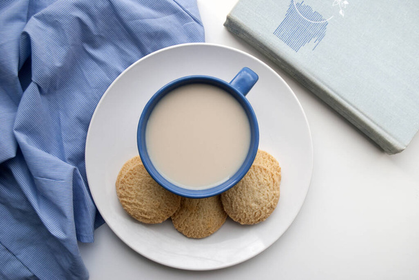 Kahvia maidolla ja kekseillä. Riisijauhoista valmistetut gluteenittomat pyöreät murokeksit. Sininen. Valkoisella pohjalla, ylhäältä
. - Valokuva, kuva