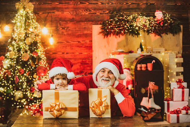 プレゼント付きの面白い小さなサンタクロースのヘルパー。サンタのヘルパー袋の贈り物でいっぱい運ぶ。サンタ・クラスに会いたい。サンタ少年は家でクリスマスを祝う. - 写真・画像