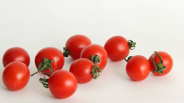 small red cherry tomatoes with green tails lie scattered on a white background red tomatoes with green tails in a glass vase on a white background close up - Φωτογραφία, εικόνα