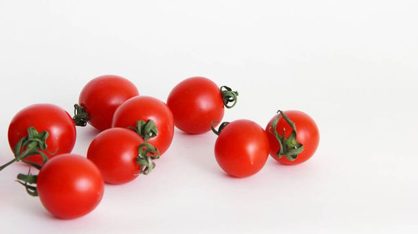 small red cherry tomatoes with green tails lie scattered on a white background red tomatoes with green tails in a glass vase on a white background close up - Foto, Imagem