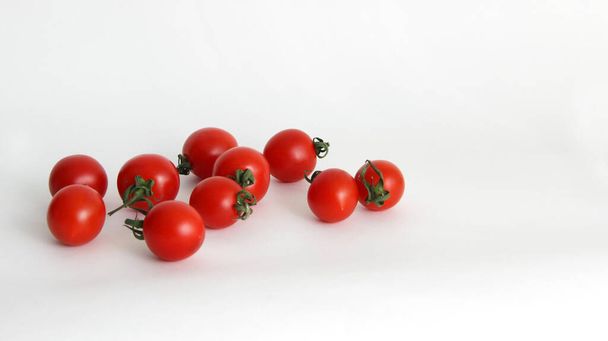 small red cherry tomatoes with green tails lie scattered on a white background red tomatoes with green tails in a glass vase on a white background close up - Foto, Bild
