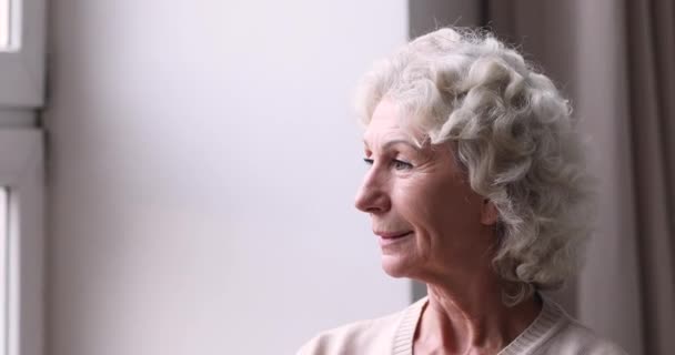 Smiling senior grandma looking through window enjoys retirement life - Záběry, video