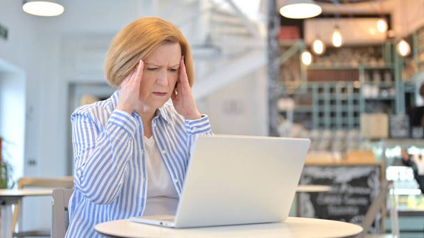 Laptop uso por mulher idosa criativa com dor de cabeça no café
 - Foto, Imagem