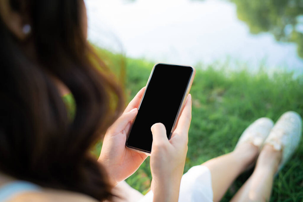 Όμορφες γυναίκες που κάθονται στο πράσινο γρασίδι χρησιμοποιούν smartphone σε απευθείας σύνδεση συνομιλία - Φωτογραφία, εικόνα