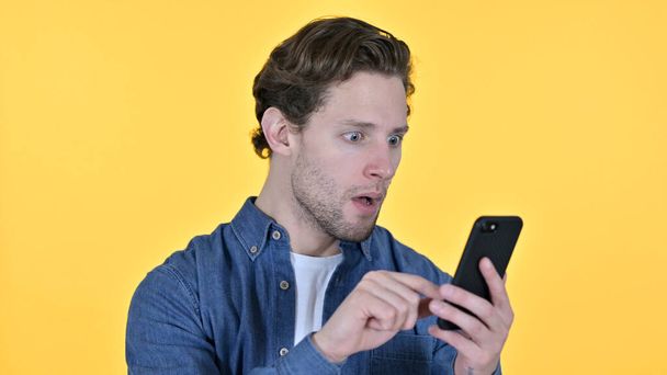 Молодой человек с потерей на смартфоне, неудача на жёлтом фоне
 - Фото, изображение