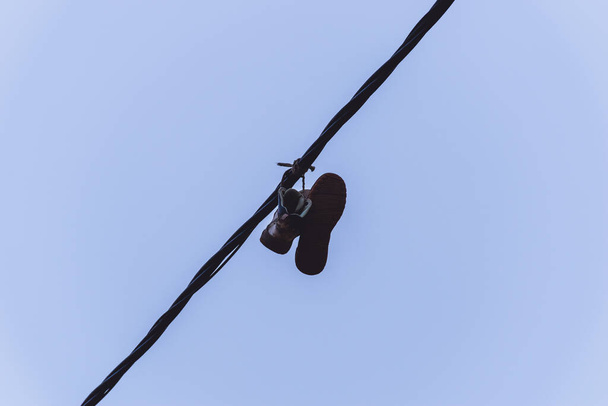 Buty turystyczne / trekingowe wiszące na linii elektrycznej wiązanej sznurówkami wysoko na tle ponurego porannego nieba - Zdjęcie, obraz