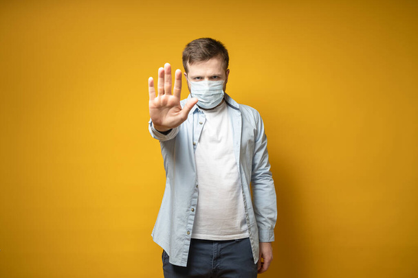 Homem sério com uma máscara médica em seu rosto faz um gesto de parada com a mão, protegendo contra o vírus. Conceito de saúde
. - Foto, Imagem