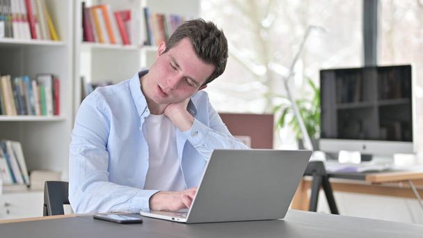 Молодий чоловік з неком болить, працюючи на лаптопі - Фото, зображення